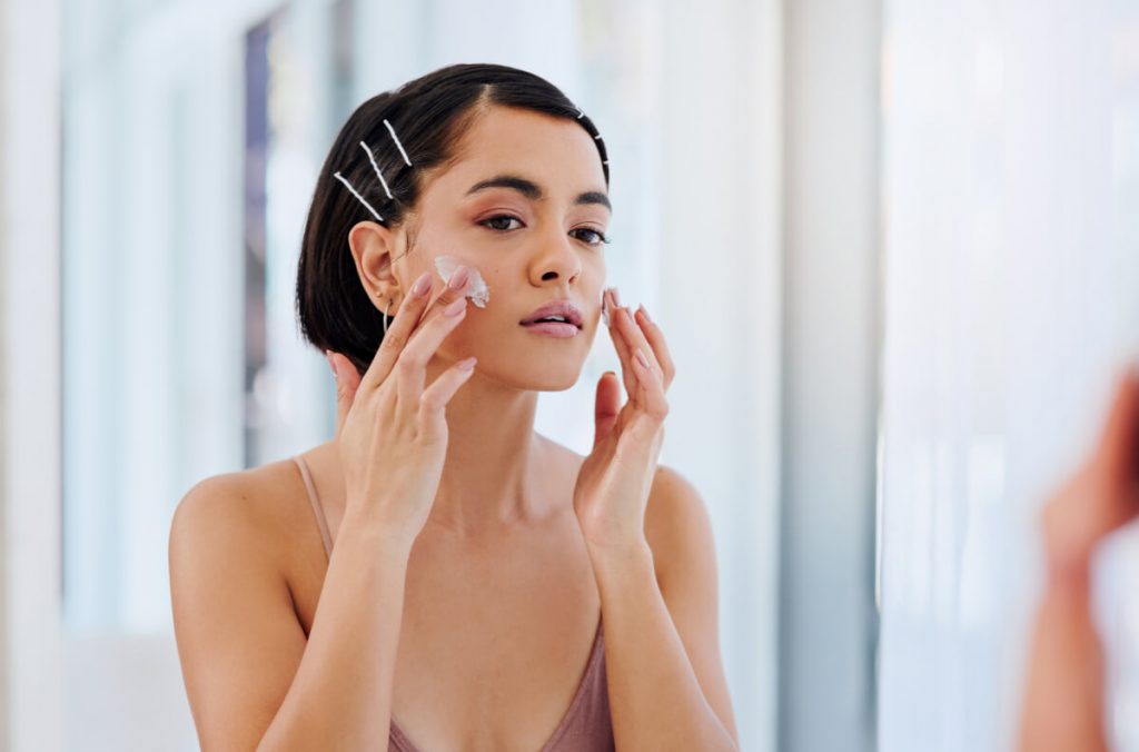 shot of an attractive young woman applying moisturiser in front of a bathroom mirror